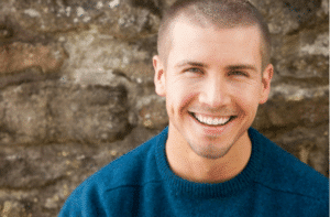 Attractive young man sitting smiling outside 300x197