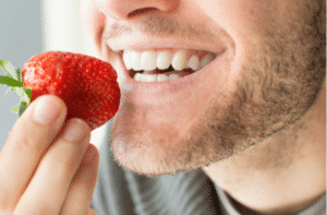 Young man holding a strawberry and smiling 300x197